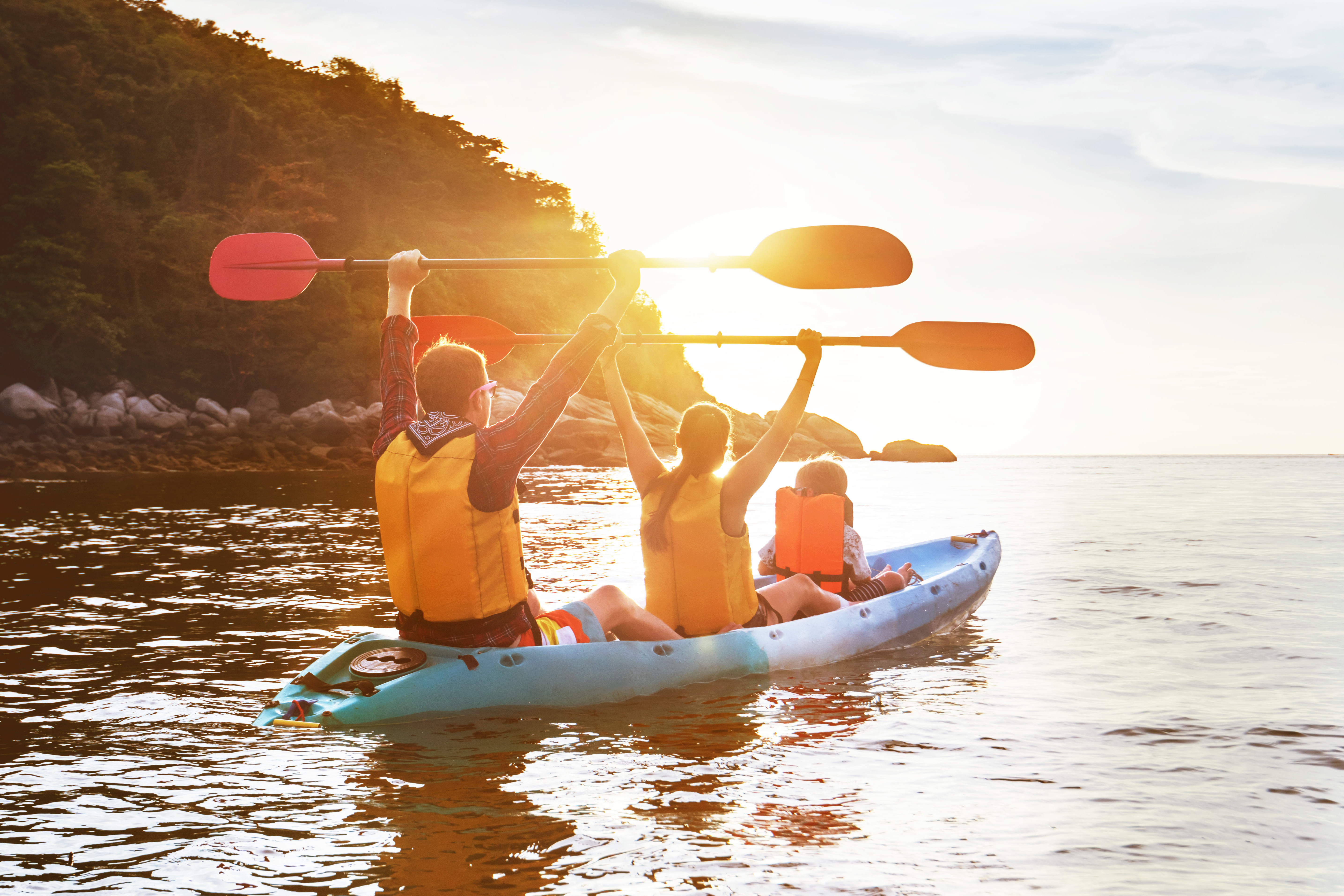 Family kayaking together with paddles raised
